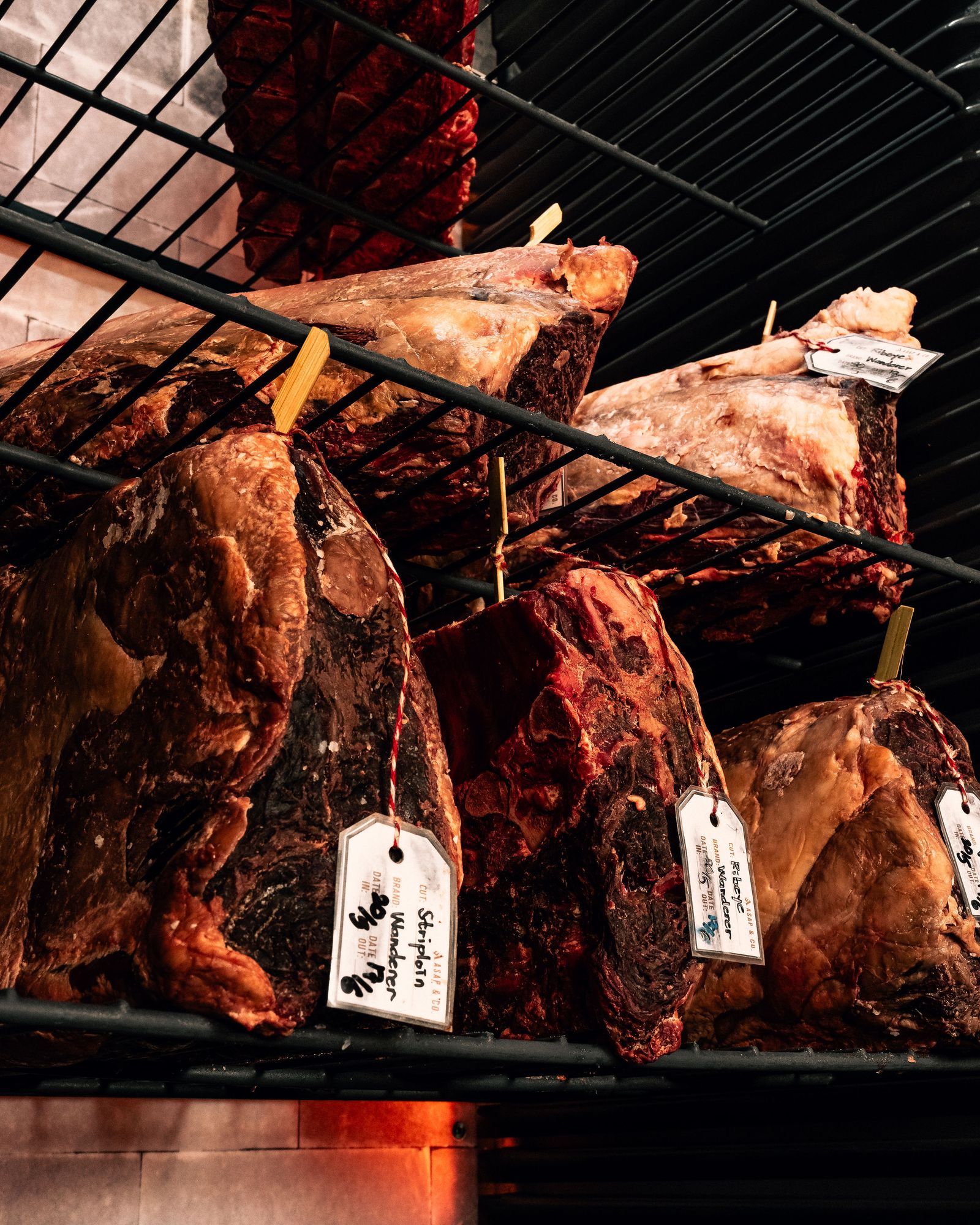 Whole cuts hanging and tagged in the dry-aging cabinet